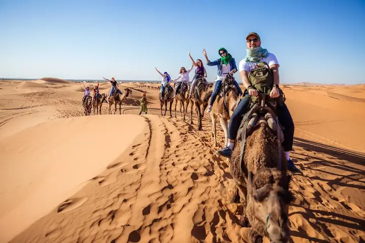 Viajeros saludando desde sus camellos en Merzouga