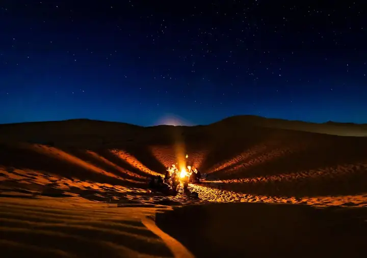 Hoguera encendida entre las dunas bajo el cielo nocturno